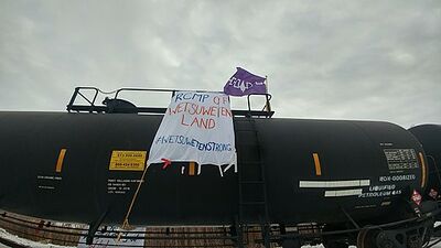 A banner painted with the words "RCMP OFF WET’SUWET’EN LAND" and the hashtag #WETSUWETENSTRONG in blue and red lettering, as well as a Haudenosaunee flag on a stopped liquefied petroleum gas tank car in Vaughan, Ontario, at a protest event on February 15, 2020 in solidarity with Wet’suwet’en hereditary chiefs opposing the Coastal GasLink Pipeline.
