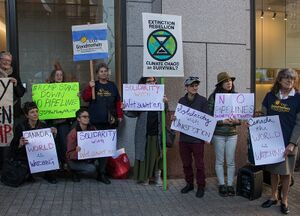 A group of people stand in front of a building with various protest signage that include slogans in support of Wet'suwet'en.