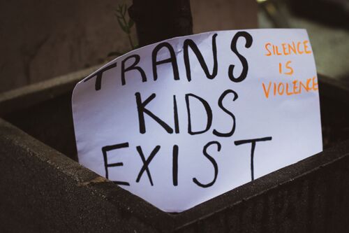 Black and white sign that reads: Trans Kids Exist - Silence is Violence